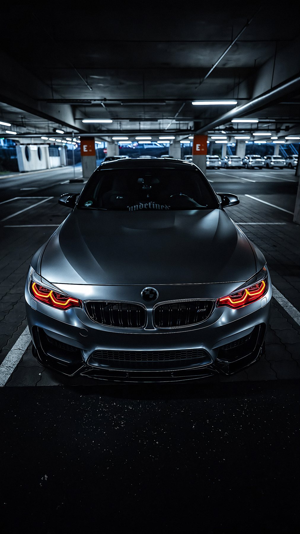 EMIRSHARK BMW M3 F80 in Mattsilber, Frontansicht mit leuchtenden roten Angel Eyes in dunkler Tiefgarage